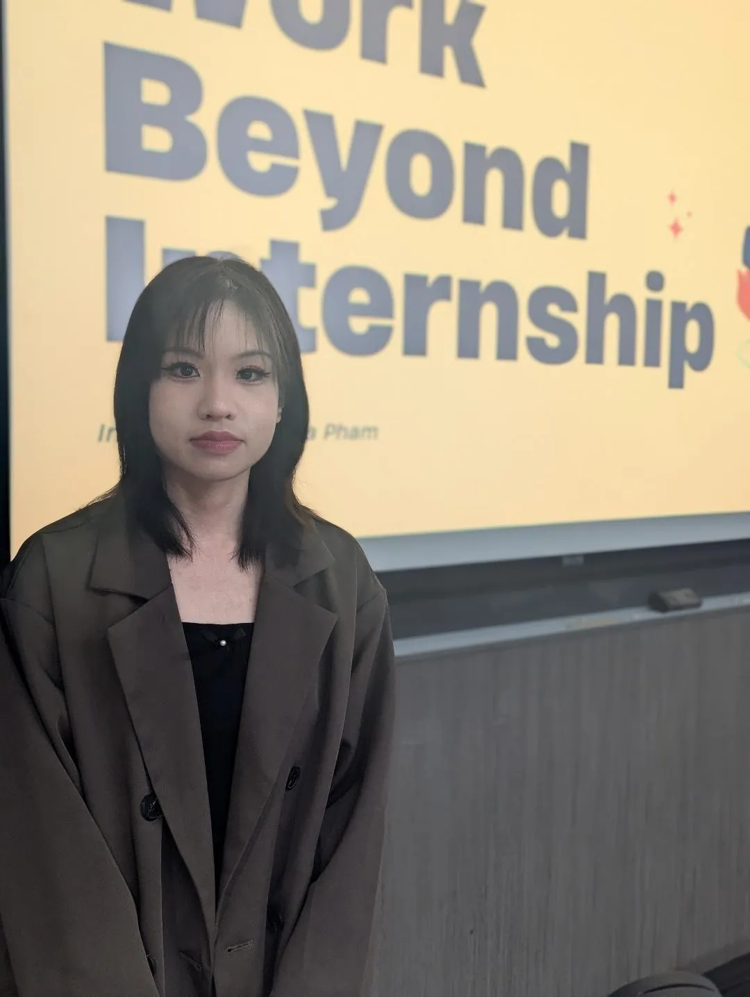 Victoria Thuylinh Pham presenting in a classroom beside a projected slide.